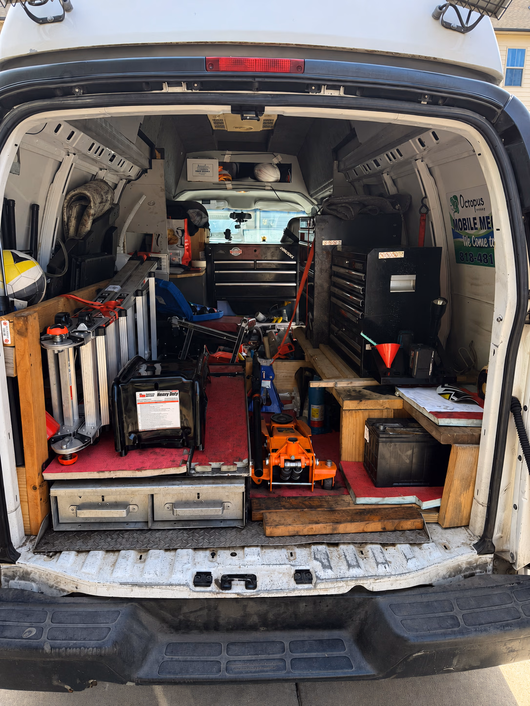 Open back of a white work van filled with tools, ladders, toolboxes, and equipment for repairs.